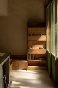 A cozy living area with a wooden bookshelf in front of a window, surrounded by books and a bench for reading or relaxation