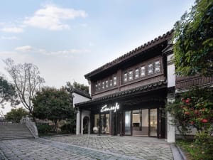 A traditional Asian building with a large wooden structure, tile roof, and archway leading to a courtyard, surrounded by potted plants