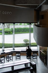 Calm and inviting living-dining space with natural light, wood, and glass, featuring a man sitting at a desk in front of a window