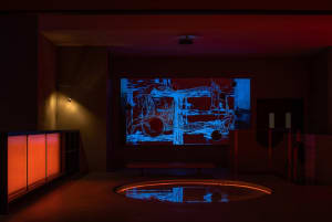 A modern art gallery with a digital artwork displayed on a large screen, featuring a bench and decorative bowls in a contemporary and creative environment