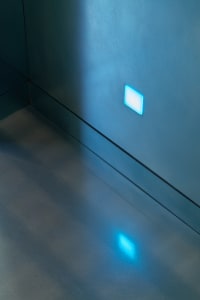 Well-lit room with a silver floor, blue wall lights, and a chair in a modern office or living area with a clean and minimalistic atmosphere