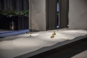 A modern space with a white concrete wall featuring two golden statues at different heights, creating an artistic focal point