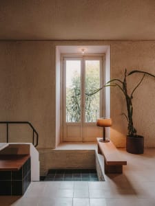 Modern bathroom with a sink, toilet, and shower area, featuring concrete walls, a large window, and a potted plant