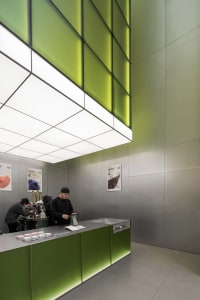 A modern restaurant interior with a metal counter, green walls, and customers ordering food and drinks