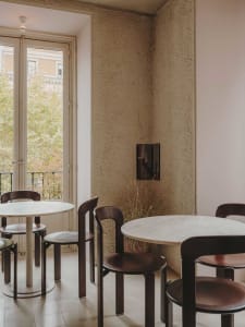 well-lit restaurant interior with tables, chairs, and potted plants, featuring a mix of brown and white tones