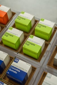 A colorful display of coffee boxes in a store, featuring green, orange, white, and brown boxes arranged on a table for an inviting and visually appealing presentation