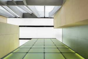 A modern interior space with a large green-tinted glass wall extending upwards, creating a sense of openness and spaciousness