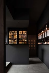 Dark wine bar with a wooden counter displaying bottles of wine, creating a cozy and intimate atmosphere for patrons to enjoy their drinks