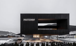 Black modern building with a glass front, natural light, and a car parked outside