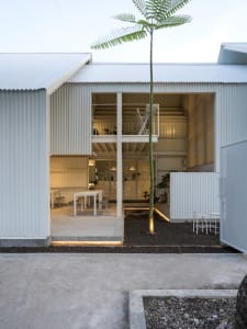 Modern house with white walls, metal roof, and patio area, featuring a staircase and outdoor seating with chairs around a dining table