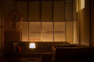 Cozy living room with a couch, chair, and lamp, featuring a wall covered in paper and a warm atmosphere