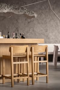 An empty bar area with wooden stools and tables, featuring a selection of bottles on the counter, creating a calm and inviting atmosphere