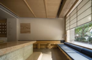 Empty room with wooden walls and floors, featuring a bench along one wall and another in the corner, with two chairs near the center, creating a calm and serene atmosphere