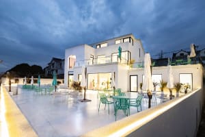 A large white house with modern design, clean lines, and minimalistic elements, featuring multiple balconies and patios with outdoor furniture