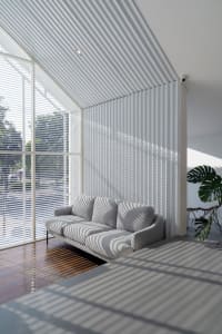 Open living area with a striped sofa, vertical blinds, potted plants, and a chair, featuring natural light and a simple atmosphere