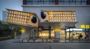 Modern building with a scissor-like design, featuring a large window and seating areas, set against a neutral background