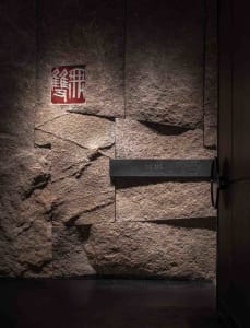 Traditional Asian interior with a stone wall featuring Chinese characters, wooden doors, and a rustic atmosphere