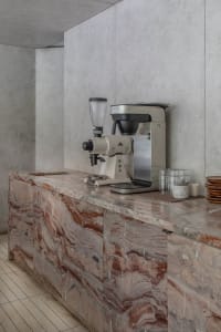 A modern kitchen with a marble countertop featuring two coffee makers and three cups arranged in different locations