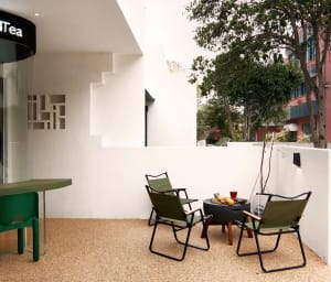 A relaxed outdoor patio with brick flooring, two chairs, two dining tables, and potted plants, perfect for al fresco dining or relaxation