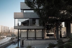 A modern building with gray stone walls and black glass windows, set against a backdrop of trees in an urban environment