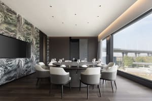 A modern dining area with a round table, chairs, and fine dining setup, set against a wood-floored background