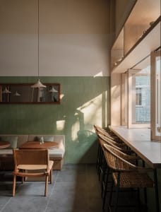 A modern restaurant interior with green walls, multiple tables, chairs, couches, and a bar counter, creating a warm and inviting atmosphere