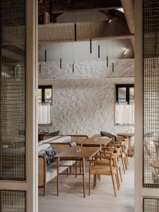 A modern restaurant interior with a large dining area featuring multiple tables and chairs, vases, and warm lighting