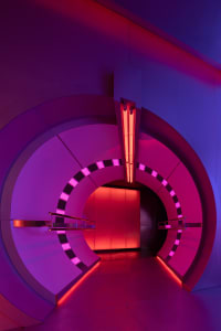 A futuristic interior space with a spiral staircase, pink and purple walls, and red lights on the staircase