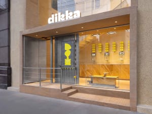 Modern office space with a glass door, chairs, a dining table, and a bench, featuring a well-lit and functional atmosphere