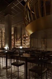 A cozy bar area with wooden tables and chairs, featuring bottles and wine glasses, set in a warm and inviting atmosphere