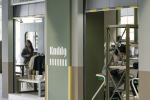 A modern office space with a green wall, chairs, and a dining table, featuring people socializing and working