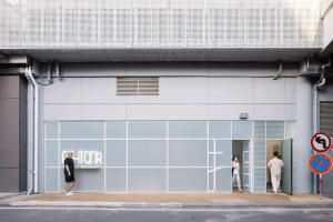 Casual street scene with people looking at a building with a large window that says PHIONR