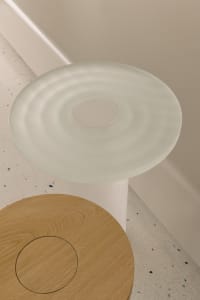 A modern space with a minimalist style featuring a circular glass table on a wooden base in front of a white wall