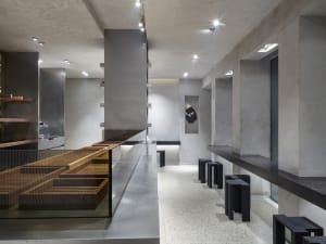 Modern restaurant interior with a large counter, gray and brown tones, stools, and decorative items, highlighted by lighting