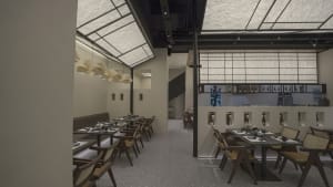 A modern restaurant interior with multiple tables, chairs, and benches in a dimly lit space with white and brown tones on the walls