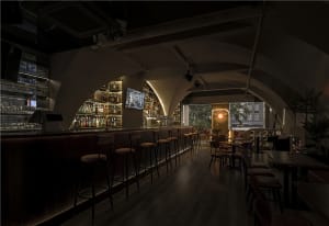 Empty bar area with wooden floors and walls, featuring chairs and bottles, creating a quiet and inviting atmosphere
