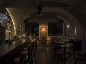 A bar area in a restaurant with wooden chairs and tables, a counter, and bottles of beverages, creating a welcoming atmosphere for socializing