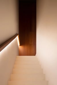 A traditional staircase with wooden steps and a white railing, illuminated by a light at the bottom step, creating a warm atmosphere
