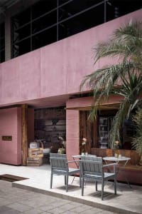Dimly lit restaurant interior with pink walls, wooden floors, and furniture, featuring bottles and a cozy atmosphere