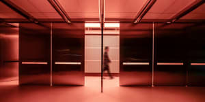 A well-lit office hallway with two open doors, a man in a suit walking through, and wooden accents on the walls and floors