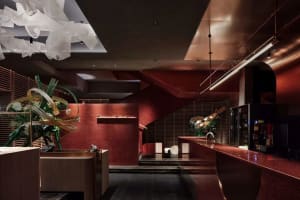 A modern lobby with red walls, wooden floors, and two large vases, well-lit and warm, with stairs in the middle of the room