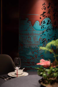 Dining area with oriental design, potted plants, and a wine glass on a table, set against a striking oriental wall design