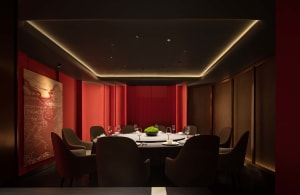 A luxurious dining area with a round table, wine glasses, plates, and cutlery, surrounded by multiple chairs in a warm and cozy red-themed space