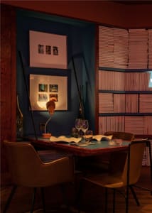 Cozy dining area with a wooden table, blue wall, and scattered books, featuring a modern style with a focus on comfort and functionality