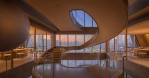 A large building with multiple levels, glass walls, and a wooden staircase, allowing natural light to enter and creating a bright atmosphere