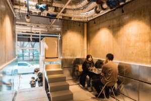 A casual restaurant dining area with concrete walls, chairs, and tables, featuring patrons enjoying meals and conversation