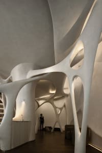 A modern art gallery with curved white walls and ceilings, featuring two people observing exhibits in a dimly lit space