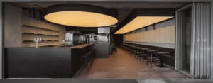 Empty modern restaurant with black walls and floors, featuring chairs and a bar, with a sleek and contemporary atmosphere