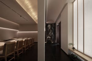 A dimly lit restaurant dining area with chairs, a dining table, and marble accents on the walls