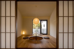 A cozy living area with a wooden floor, a round table, and three chairs, featuring a potted plant and a vase for decoration